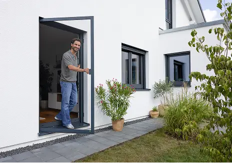 Fliegengitter-Drehtür nach Maß für Balkon und Terrasse Mann öffnet eine maßgefertigte Fliegengitter-Drehtür an einer Terrassentür