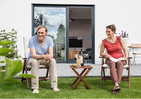Fliegengitter-Terrassentür für entspanntes Wohnen im Garten Zwei Personen sitzen im Garten vor einer Terrassentür mit Fliegengitter und genießen die Zeit im Freien