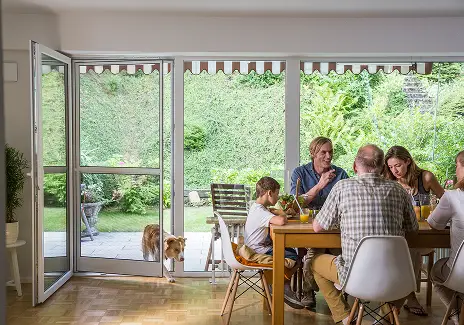 Fliegengitter-Pendeltür für Terrasse und Familienhaushalt Familie sitzt am Esstisch bei geöffneter Terrassentür mit Fliegengitter-Pendeltür