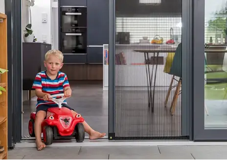 Insektenschutz-Plisseetür für einen komfortablen Durchgang zur Terrasse Kind fährt mit Rutschauto durch eine Terrassentür mit Insektenschutz-Plisseetür